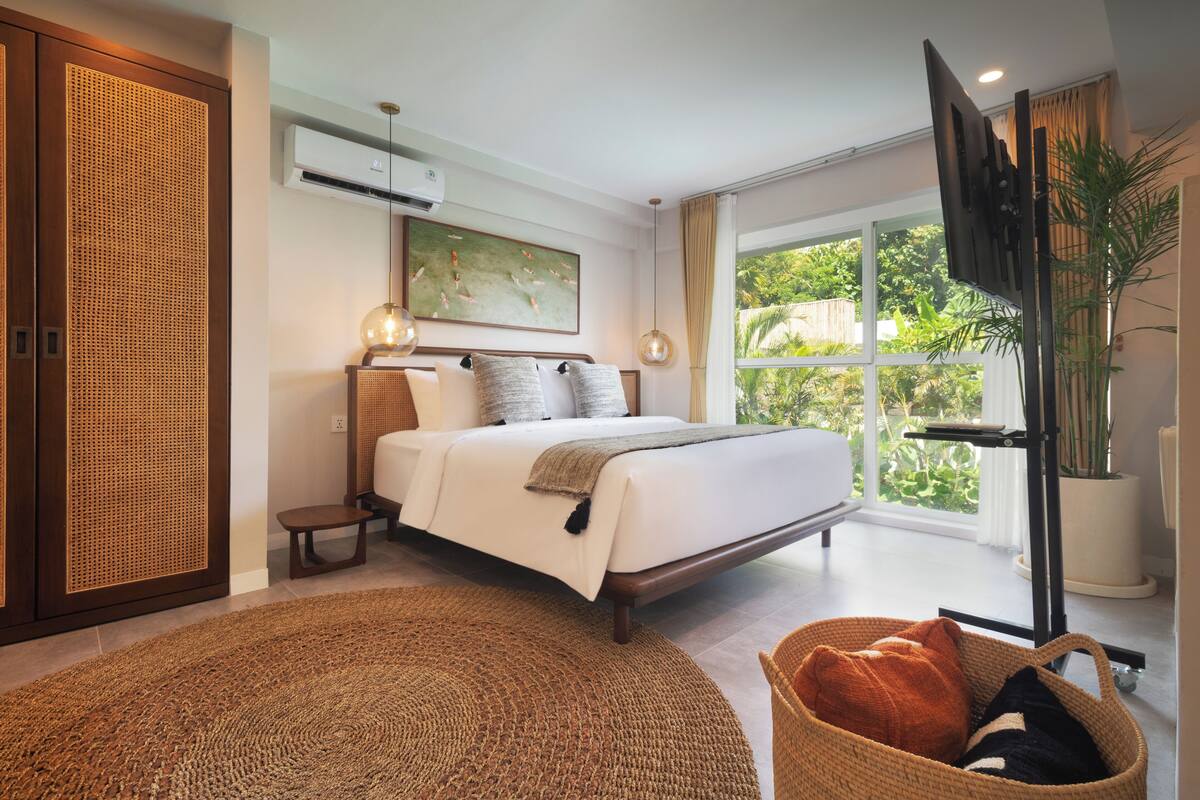 Een slaapkamer met een bed, een groot raam, een tv aan de muur en een kamerplant.