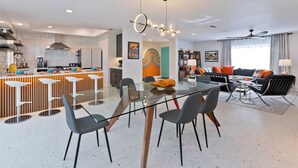 A modern kitchen with a central island, a dining area with a glass table and chairs, and a living room with a sofa and decorative pillows. - Escoba Ranch, spectacular property, large yard and citrus grove, License #064010 (Palm Springs)