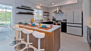 A modern kitchen with a central island, bar stools, a refrigerator, and a large window. - Escoba Ranch, spectacular property, large yard and citrus grove, License #064010 (Palm Springs)