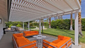 An outdoor patio with orange seating, a white pergola, and a well-maintained lawn. - Escoba Ranch, spectacular property, large yard and citrus grove, License #064010 (Palm Springs)
