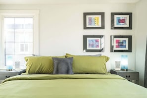 Ein Bett mit grüner Bettwäsche, zwei Nachttische mit Lampen und vier gerahmte Kunstwerke an der Wand.