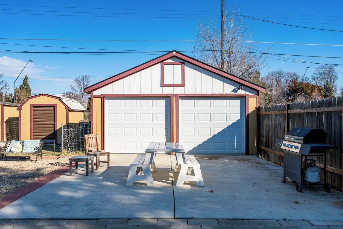 A garage with two white doors, a picnic table, and a grill outside.