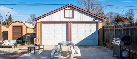 A garage with two white doors, a picnic table, and a grill outside.