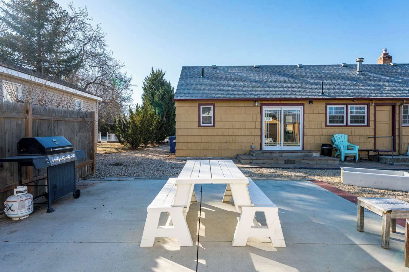 Un jardin avec une table de pique-nique, un barbecue et un petit bâtiment doté d’une porte et de fenêtres.