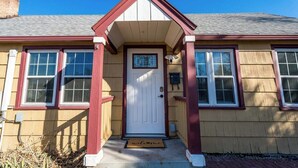 A two-story house with a white front door, a small porch with a red railing, and a chimney on the roof. - #StayinMyDistrict Depot Bench Near Downtown BSU (Boise)