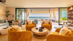 Ein modernes Wohnzimmer mit Meerblick, ausgestattet mit einer Couch, Sesseln, einem Couchtisch und einem Essbereich mit Grill.