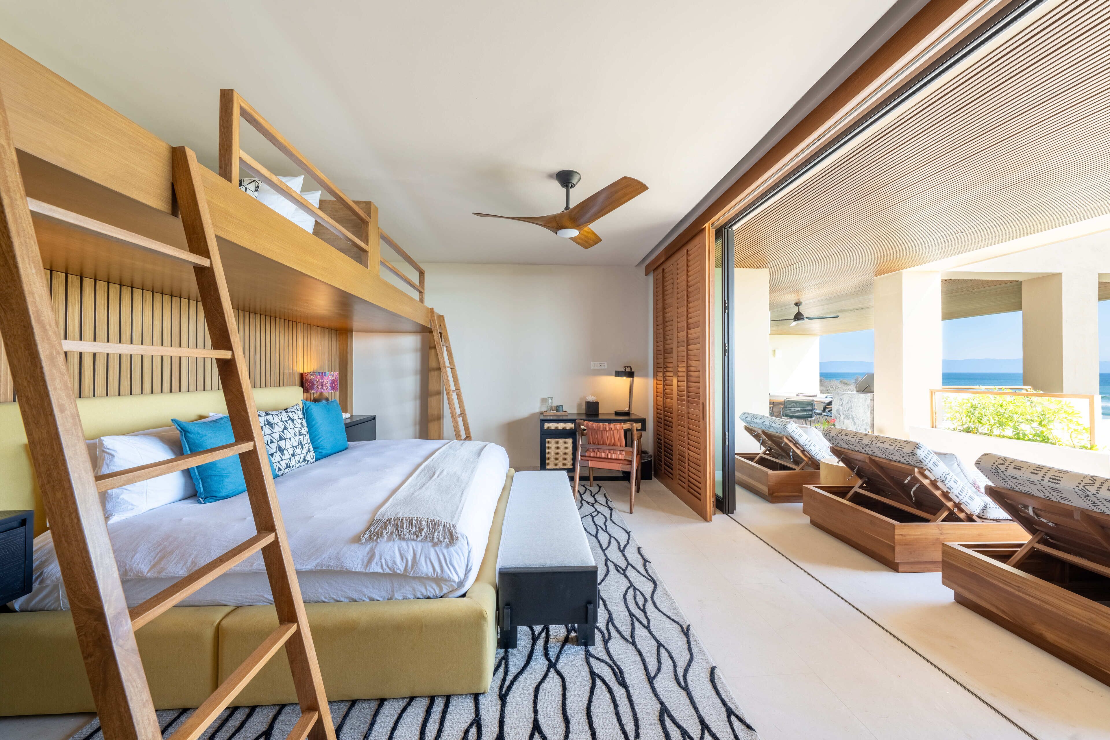 Une chambre d’hôtel moderne équipée d’un lit superposé, d’un bureau et d’un coin salon avec vue sur l’océan.