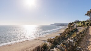 Une plage côtière bordée d’une falaise rocheuse, avec un sentier pédestre et une vue dégagée sur l’océan.