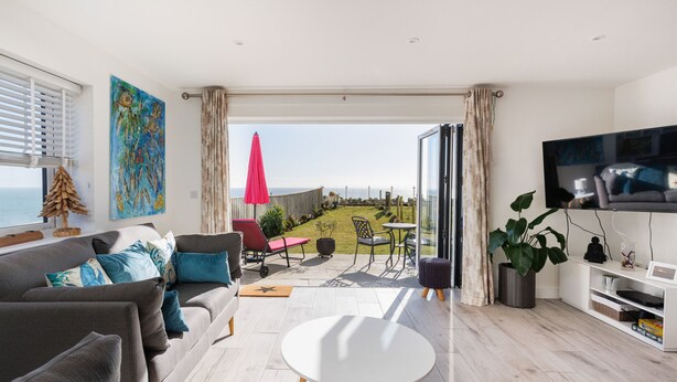 Un salon moderne avec un canapé, une table basse, un téléviseur et un balcon offrant une vue sur la mer.
