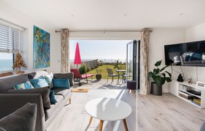 Una sala de estar moderna con sofá, una mesa de centro, televisor y un balcón con vistas al mar.