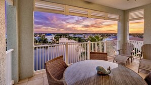 Un balcone con vista sul tramonto su una zona residenziale, mobili in vimini e una ventola a soffitto.