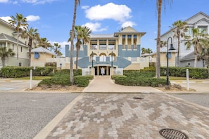 A hotel with a central entrance, palm trees, and a paved walkway.