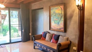 A room with a sofa, a painting, and a view through a glass door. - Baan mansin (Pak Chong)