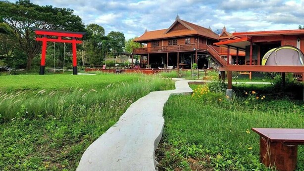 A traditional wooden building with a covered porch and a red torii gate in a lush garden setting. - Baan mansin (Pak Chong)