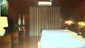 A hotel room with a bed, a nightstand, a lamp, a mirror, a window with curtains, and a wall-mounted air conditioner. - Baan mansin (Pak Chong)
