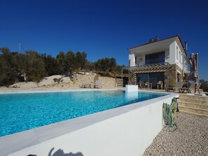 Una villa moderna con piscina, mobiliario de exterior y un muro de piedra.