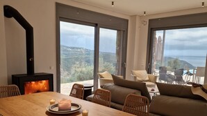 Een moderne woonkamer met een grote houten eettafel, rieten stoelen, een bank en een open haard.