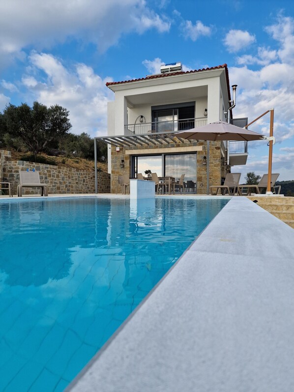 Una casa moderna con piscina, muros de piedra y un balcón con mobiliario exterior.