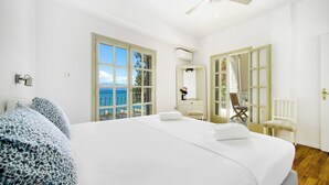 A hotel room with a large bed, a ceiling fan, and a view of the sea through large windows.