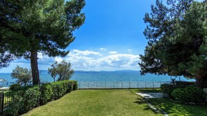 A grassy lawn with a pathway leading to a body of water, surrounded by trees and a fence.