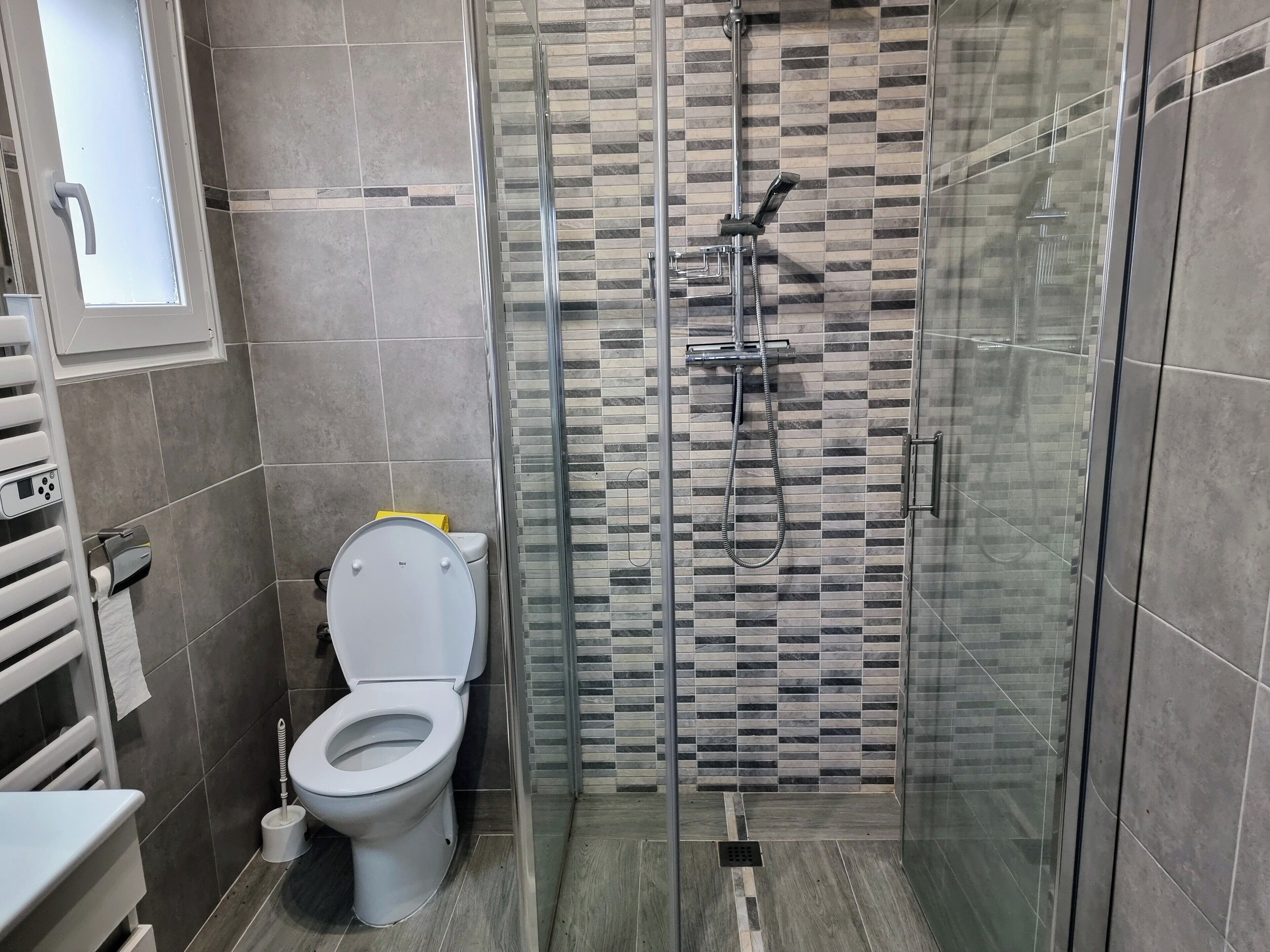 A modern bathroom with a glass-enclosed shower, a toilet, and a towel rack.