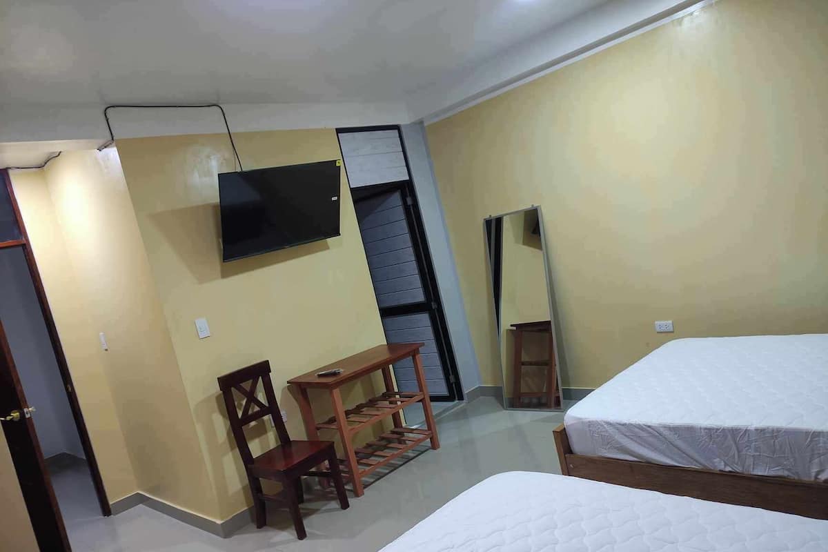 Ein Hotelzimmer mit zwei Betten, einem Fernseher, einem Holzstuhl und einem kleinen Tisch.