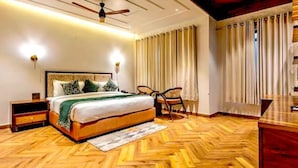 A bedroom with a wooden herringbone floor, a bed with a headboard, a ceiling fan, and a nightstand. - The Nathuli Manor (Mussoorie)