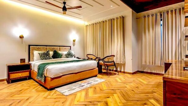 A bedroom with a wooden herringbone floor, a bed with a headboard, a ceiling fan, and a nightstand. - The Nathuli Manor (Mussoorie)