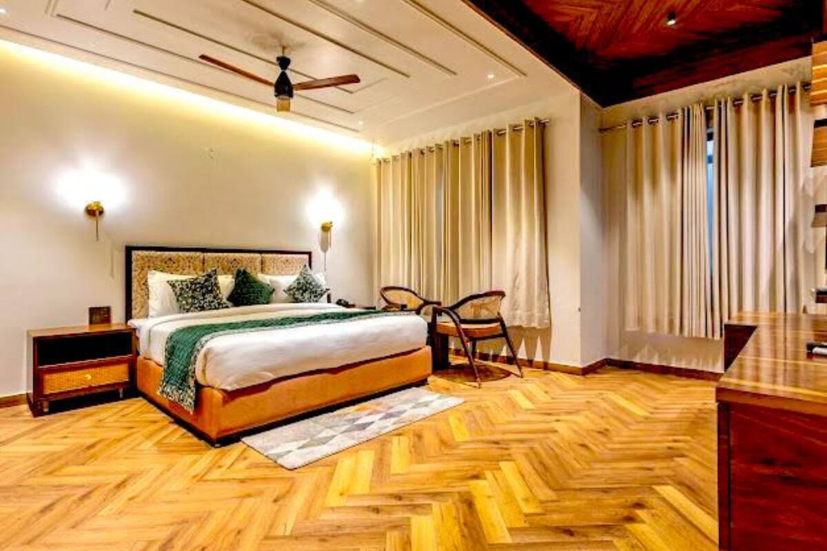 A bedroom with a wooden herringbone floor, a bed with a headboard, a ceiling fan, and a nightstand.