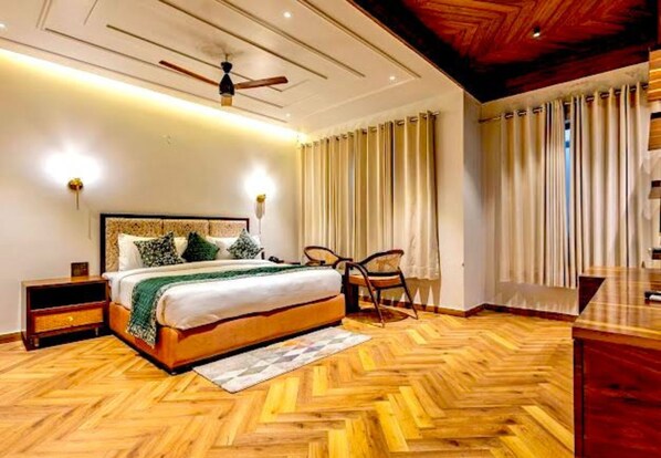A bedroom with a wooden herringbone floor, a bed with a headboard, a ceiling fan, and a nightstand. - The Nathuli Manor (Mussoorie)