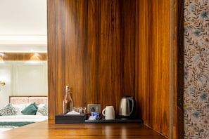 A hotel room with a wooden panel wall, a bedside table with a bottle, glasses, a tissue box, a kettle, and a tray with a cup.