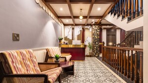A reception area with a reception desk, a sofa, a patterned rug, and a staircase with wooden railings. - The Nathuli Manor (Mussoorie)