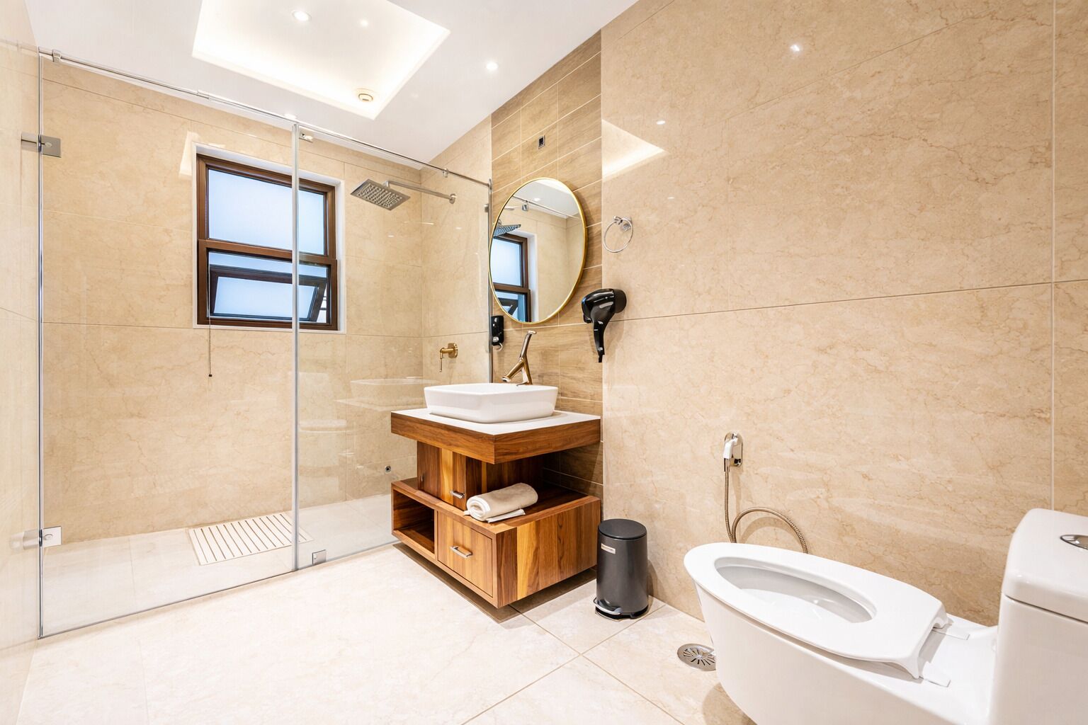 A modern bathroom with a glass shower enclosure, a wooden vanity, a toilet, and a large mirror.