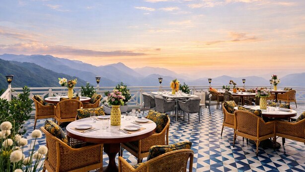 A terrace with round tables and wicker chairs, overlooking a mountainous landscape. - The Nathuli Manor (Mussoorie)