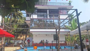 Área de piscina com um edifício de dois andares ao fundo, cercada por palmeiras.