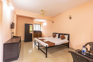 A hotel room with a bed, a desk, a wardrobe, a television, and a ceiling fan. - Colours fly Hotel  (Colva)
