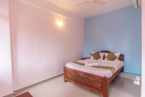 A bedroom with a wooden bed, pillows, and a bedside table. - Colours fly Hotel  (Colva)
