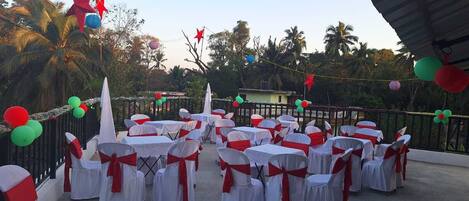 An outdoor event space with tables and chairs arranged for a gathering, surrounded by a fence and decorated with balloons and star-shaped ornaments.