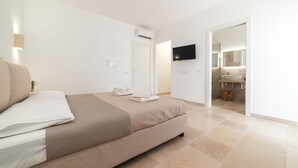 A modern bedroom with a bed, a flat-screen TV, and a bathroom visible through an open door. - Stunning luxury retreat with large pool. Great location near the sea in Puglia (Carovigno)
