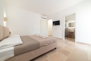 Ein modernes Schlafzimmer mit einem Bett, einem Flachbildfernseher und einem durchgegangene Tür erkennbaren Badezimmer.