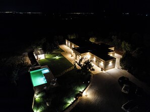 Ein gut beleuchtetes Wohnhaus bei Nacht mit Schwimmbad, Auffahrt und Garage.