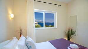 A bedroom with a bed, a window with a view of the sea, a bedside table, and a mirror. - Villa Eione-Thaleia - Lefkada Vacation (LEFKADA)