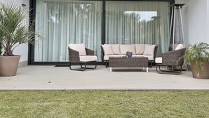 Un patio con mobiliario de mimbre, una mesa baja y plantas en macetas.
