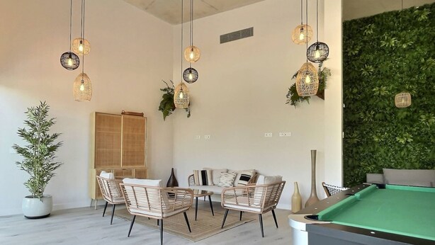Un área de estar moderna con mesa de billar, sillas de mimbre e iluminación colgante.