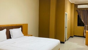 Una habitación de hotel con una cama grande, un cabecero de madera, aire acondicionado de pared y una ventana con cortinas.