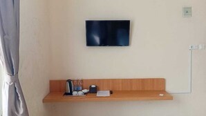 Una habitación con un televisor montado en la pared, un estante de madera con una tetera, tazas y una caja de pañuelos, y un enchufe en la pared.