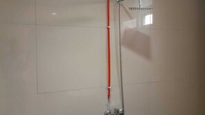 Una ducha con manguera roja, cabezal de ducha de mano y grifo empotrado.