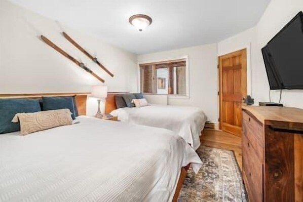 A hotel room with two beds, a wooden dresser, a TV, and a window with a view of the outside.