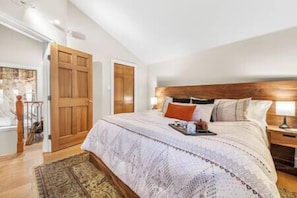 A bedroom with a large bed, wooden headboard, and a nightstand with a lamp. - Ski In/Out Retreat w/ Sauna - Telemark 7 (Whistler)