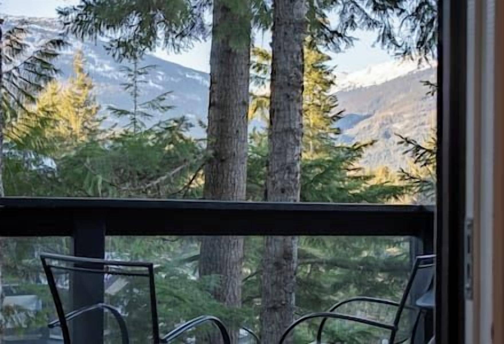 Un balcón con dos sillas, con vista a un área boscosa de árboles altos y montañas lejanas.
